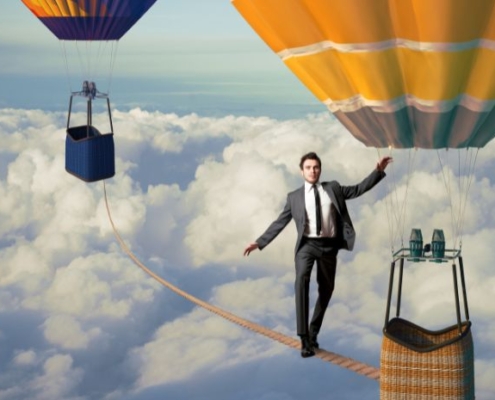 Graphic image of a man walking a tightrope between hot air balloons